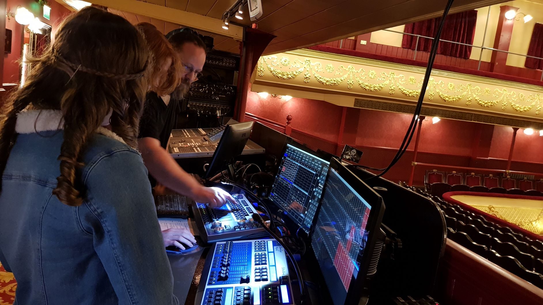 Two young people looking at lighting desk with technician