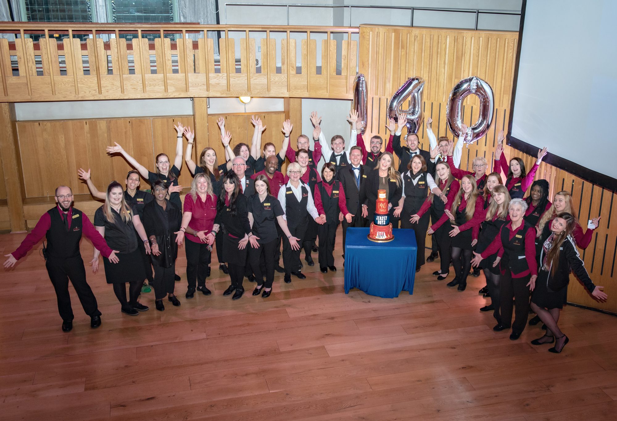 A group of Leeds Grand Theatre staff celebrating the 140th birthday with a Jersey Boys themed cake and giant 140 balloons.