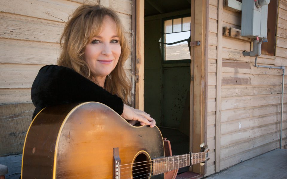 Gretchen Peters smiling and leaning on her acoustic guitar