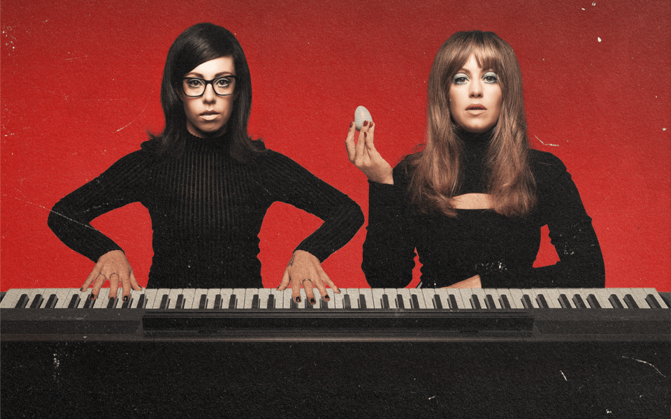 Flo And Joan sat behind a large piano wearing all black