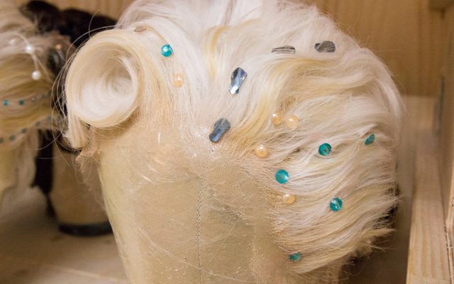 A white wig with blue and silver jewels and pearls, placed on a wig stand