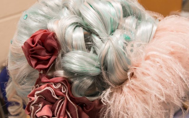 A pale pink and blue wig styled in an elegant knot with pink material and feathers around it