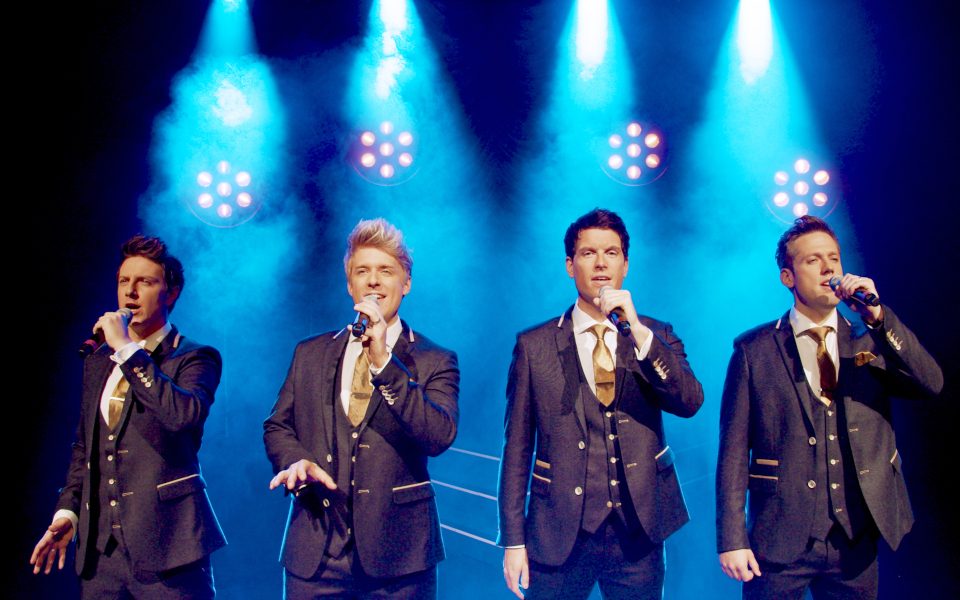 G4 - the four members wearing suits and singing into mics on stage