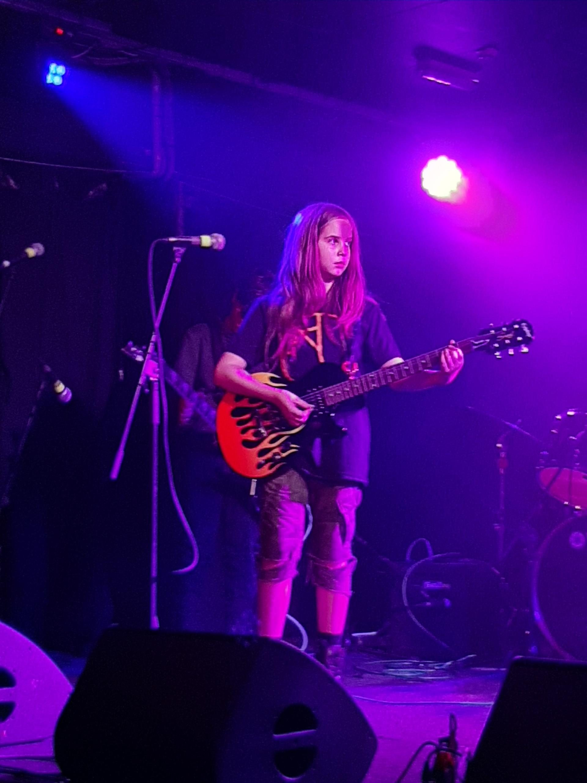 A boy with long hair playing electric guitar on stage