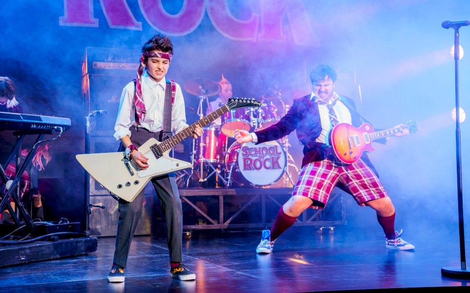 A boy playing guitar alongside Jake Sharp playing Dewey Finn