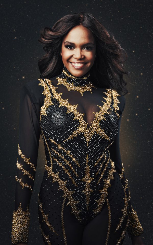 Oti Mabuse in a black and gold dance outfit smiling at the camera