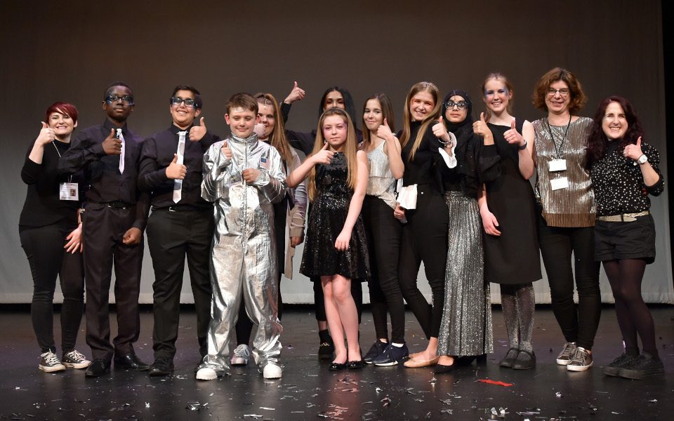 A group of young people smiling at the camera on stage