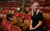 Kirsty Triplett Kirsty Triplett, wearing a black t-shirt and trousers, smiles to camera whilst sat in the auditorium at Leeds Grand Theatre