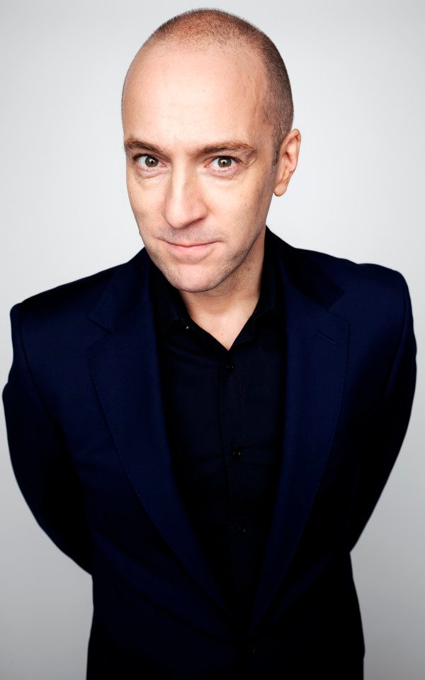 A portrait of Derren Brown against a grey background