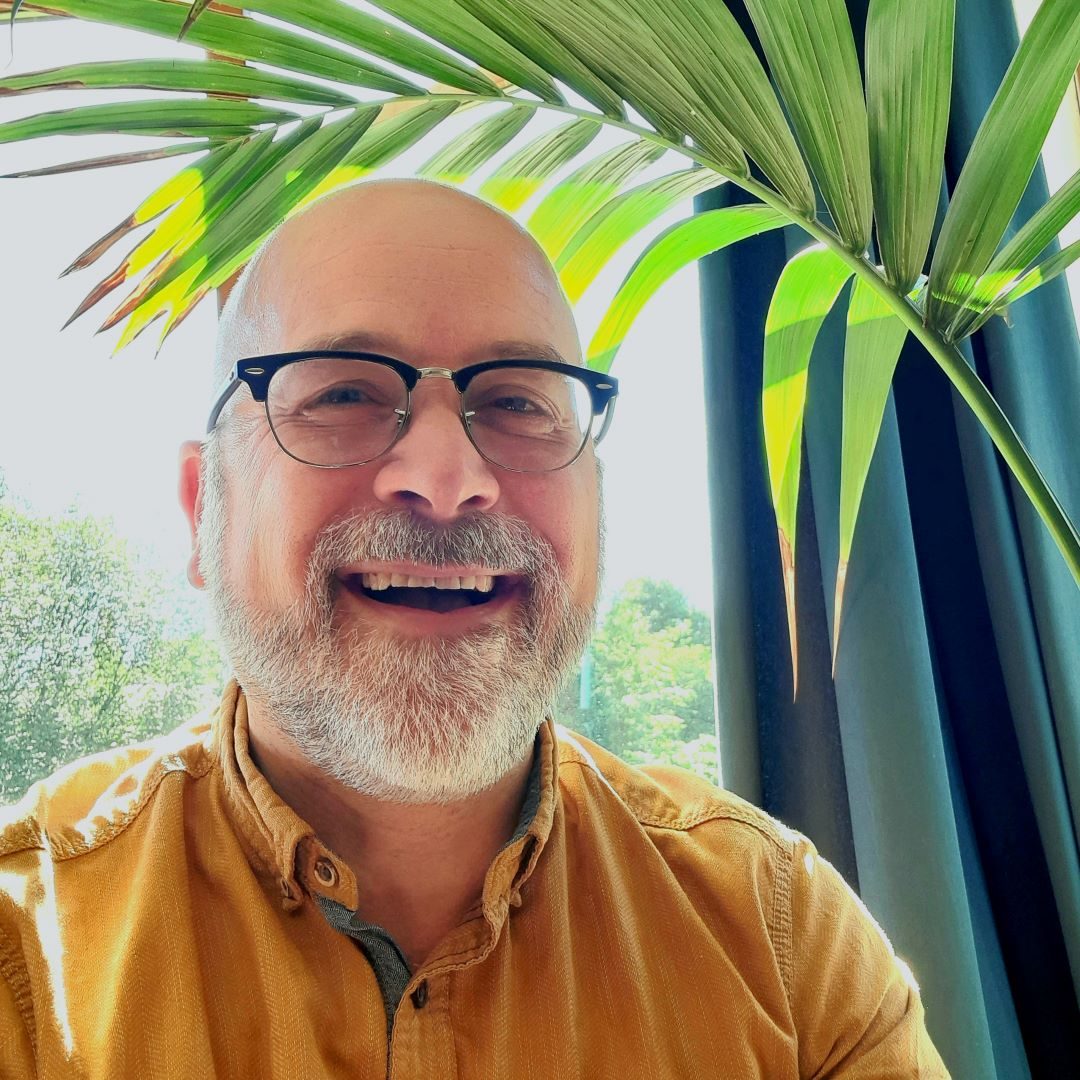 Robb Barham in glasses and an orange shirt with a green plant behind