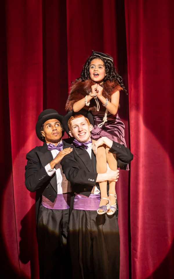 Two young men in suits holding up a young girl on their shoulder
