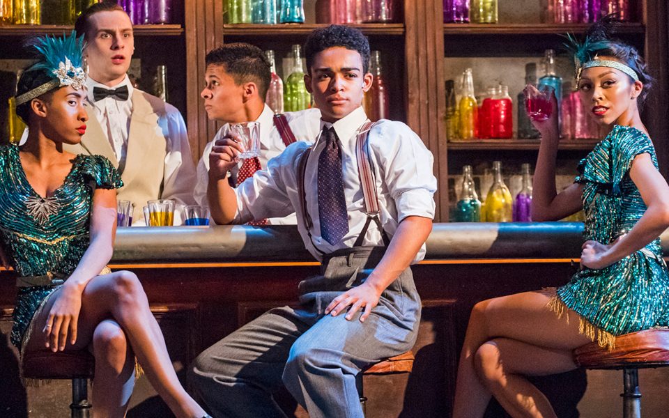 Three people dressed in 1920s costumes sitting on stools in front of a bar