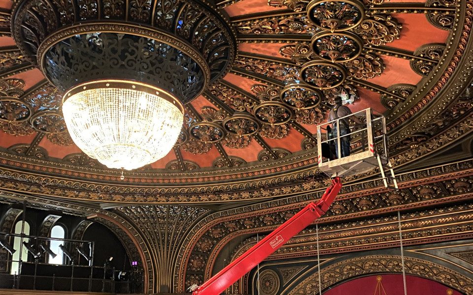 A man is in a crane and is inspecting the ornate plasterwork ceiling.