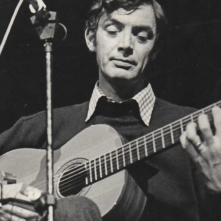 Jake Thackray playing an acoustic guitar on stage