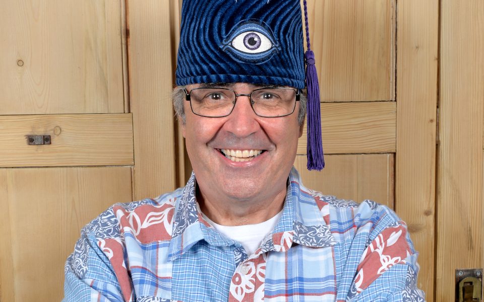 Danny Baker smiling and wearing a blue fez with an eye on it