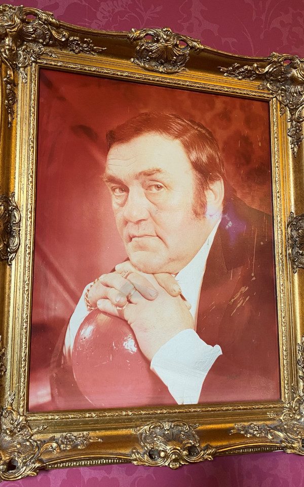 A portait of Les Dawson resting his head on his hands on a ball
