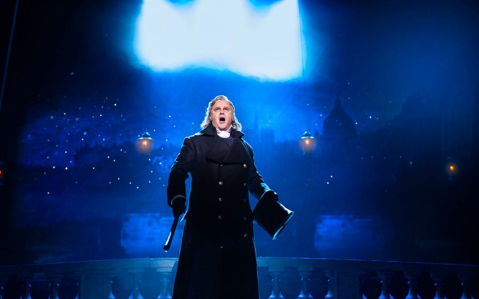 Javert in a long black coat against a night backdrop