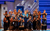 Mamma Mia! A group of people clustered together reaching out towards the audience in front of a white house
