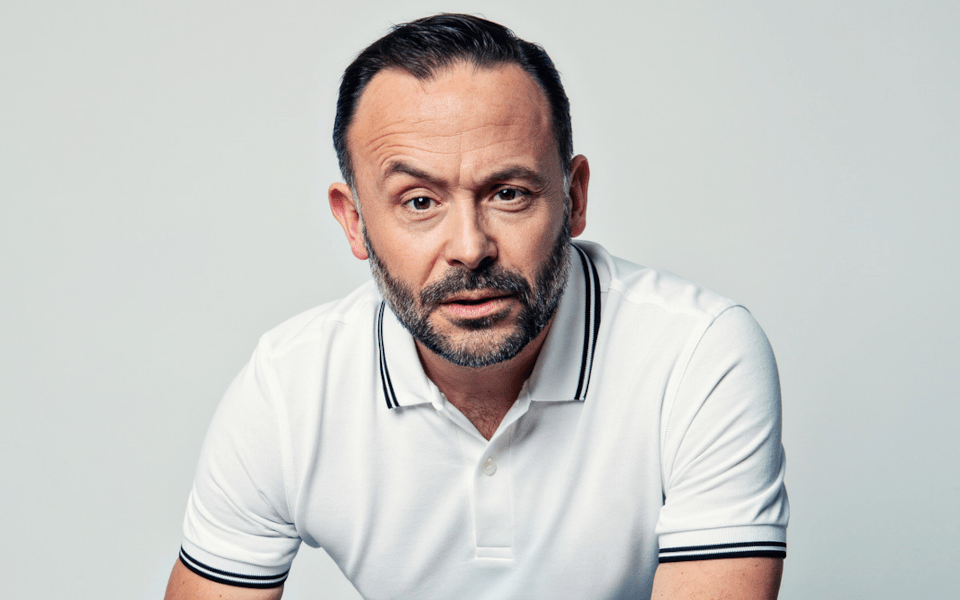 Geoff Norcott wears a white polo shirt in front of a white background.