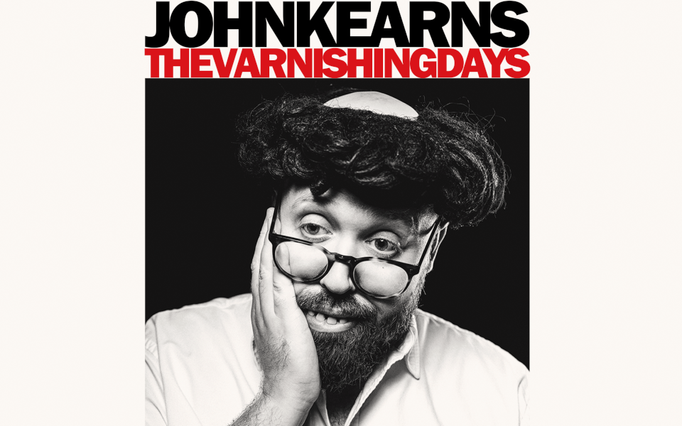 John Kearns wearing a wig and fake teeth with glasses on.