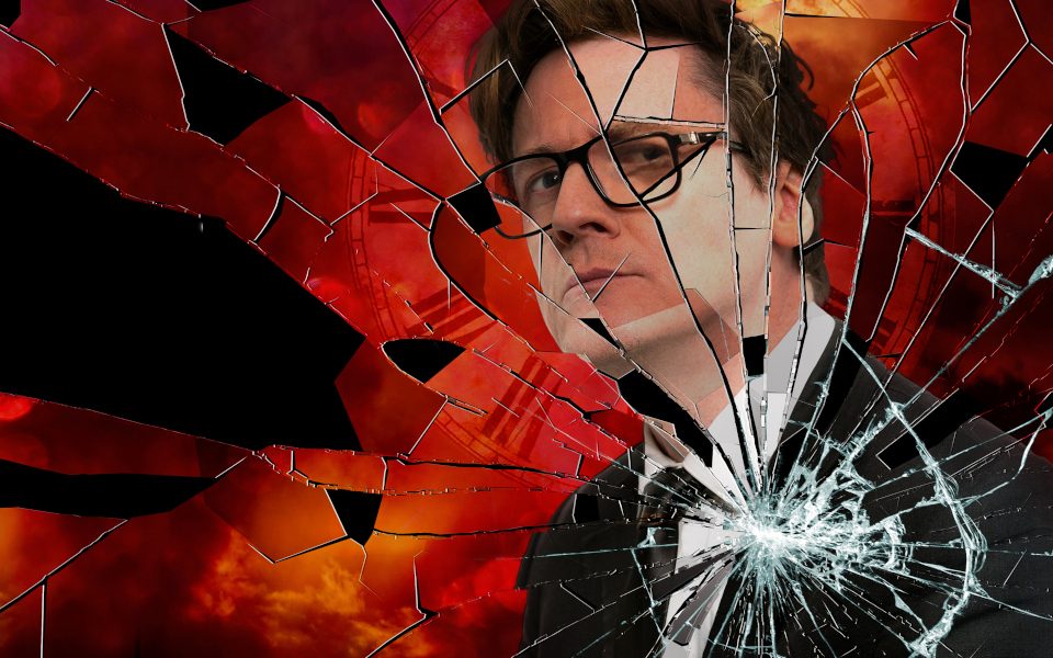 Ed Byrne is wearing glasses and a black suit. The background is a red sky with a clock faded behind. The image seems to be a smashed mirror with cracks spreading throughout.