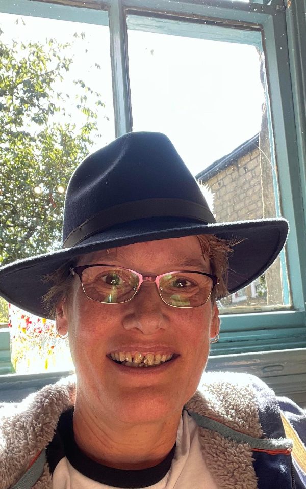 Jaki Taylor in front of a window with a fedora hat on.