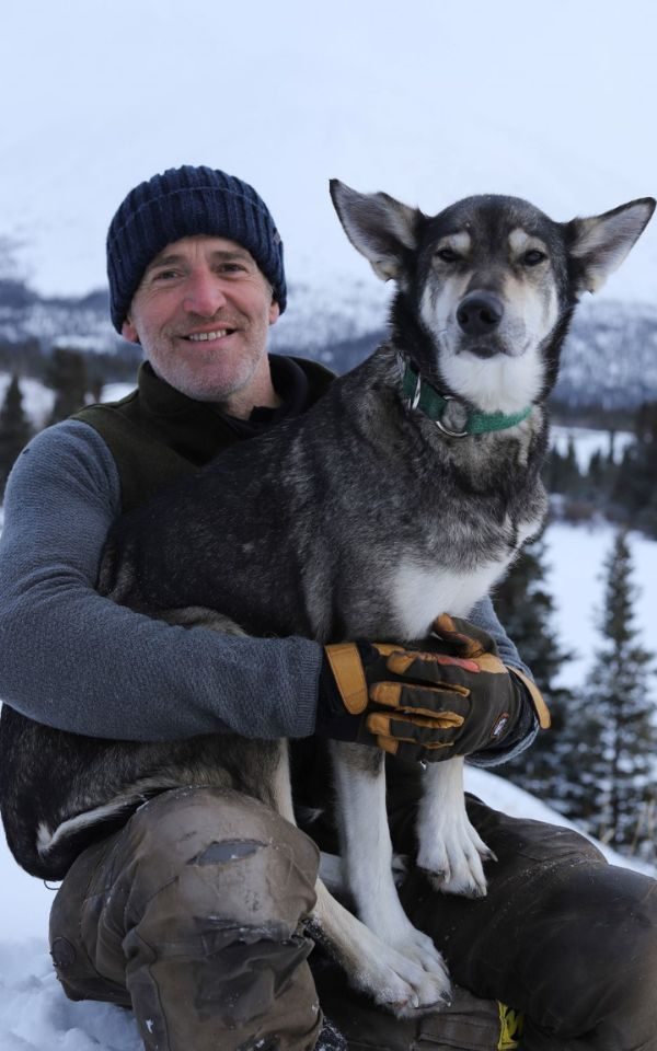Gordon Buchanan in front of a snowy landscape holding a dog on his knee