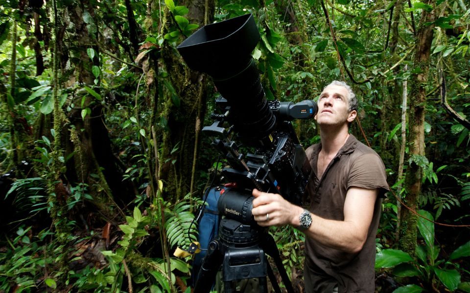 Gordon Buchanan looking up and focusing a large film camera in the middle of a jungle