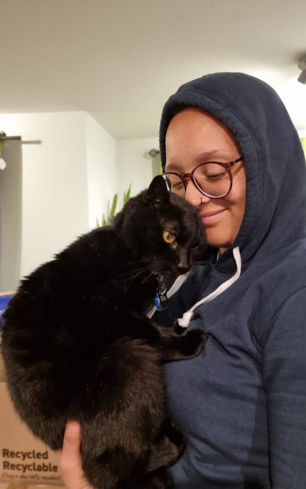 Mosa is wearing a navy jumper and holding her black cat, Tia.