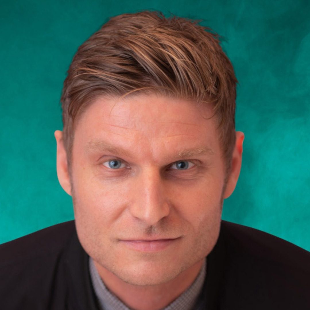 Scott Bennett is wearing a black jacket and looking at the camera. He is sitting in front of a green background.