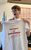 Paul Watt Paul is photographed with merchandise from Everybody's Talking About Jamie. Paul is a holding a water bottle with the logo and a white shirt with red writing on it that reads,