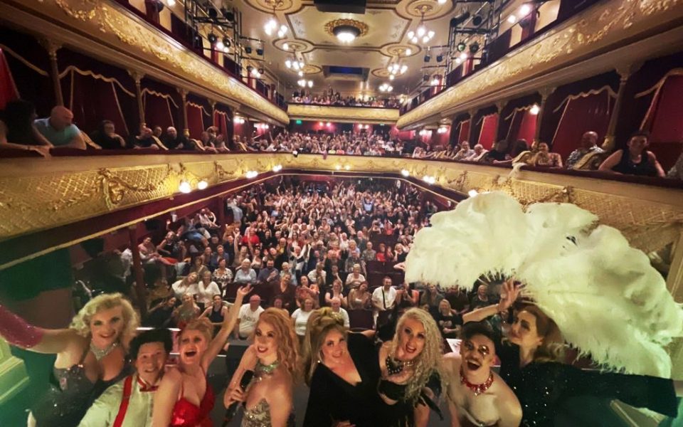 A selfie of the cast of An Evening of Burlesque with a full audience in the City Varieties auditorium behind them