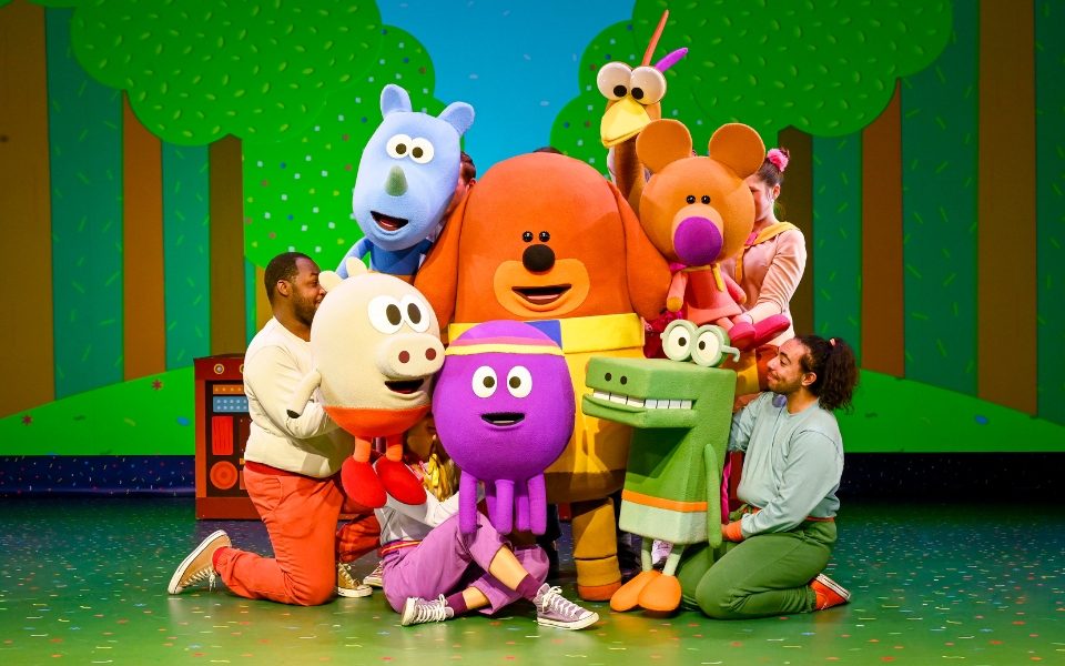 The Hey Duggee puppets and puppeteers in front of a background with cartoon trees.