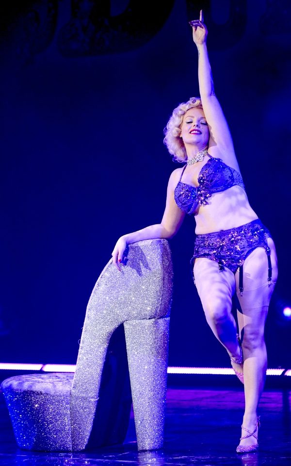 A woman in lingerie leaning on a giant sparkly silver shoe