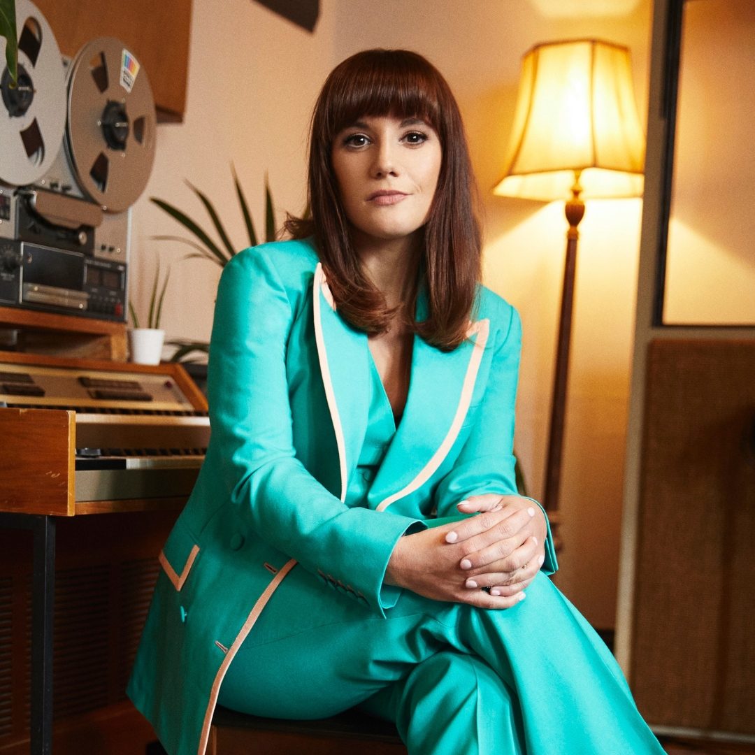 Vikki Stone sat on a piano school in a turquoise suit.