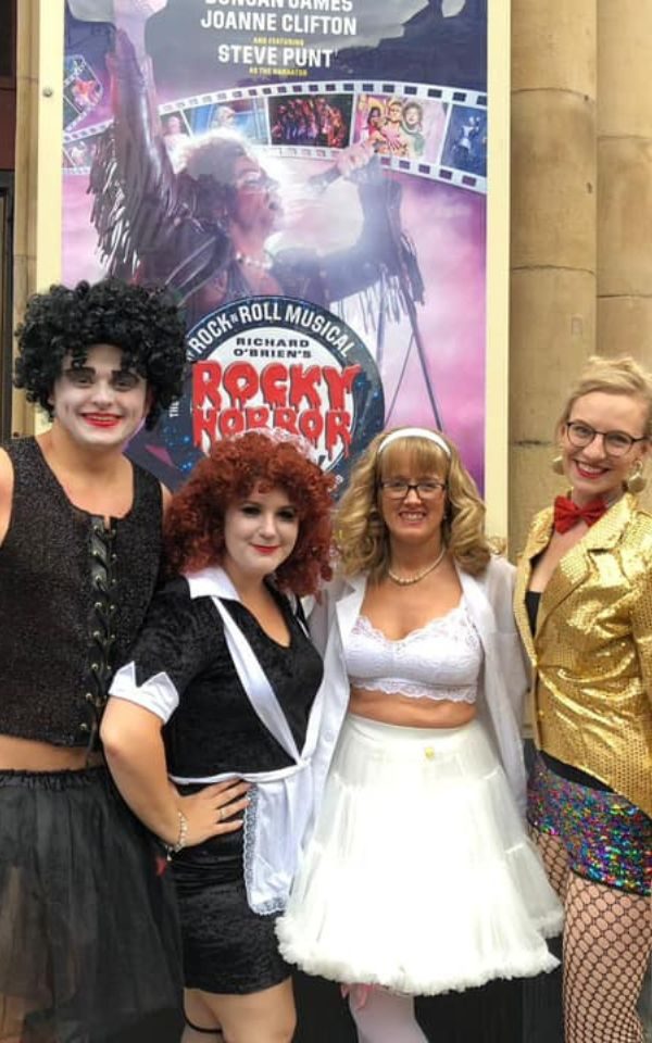 A group of friends posing in front of a Rocky Horror Show poster, all dressed as the lead roles from the show. Credit: Kate FW