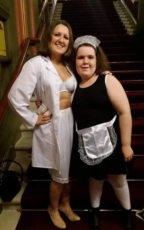 Two fans pose in The Grand in front of the stage, one in white undergarments as Janet and one in a maid's costume. Credit: Emma Lou