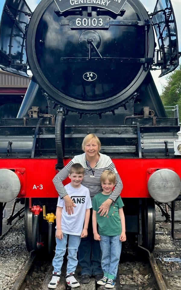 Judith Baker poses with her two grandsons in front of a train.