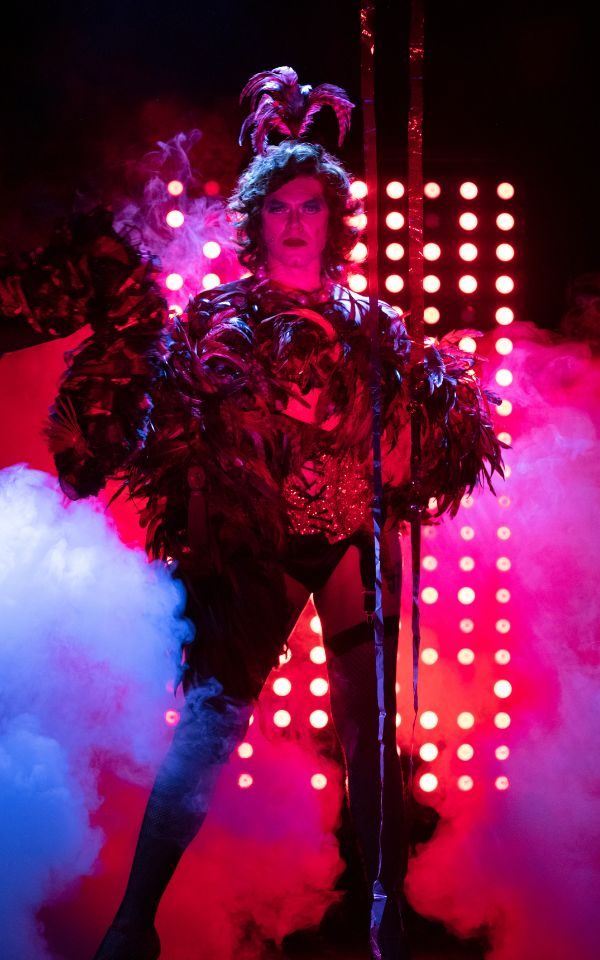 In the iconic fishnets and leather costume, Frank-N-Furter poses, backlit and washed in red light.