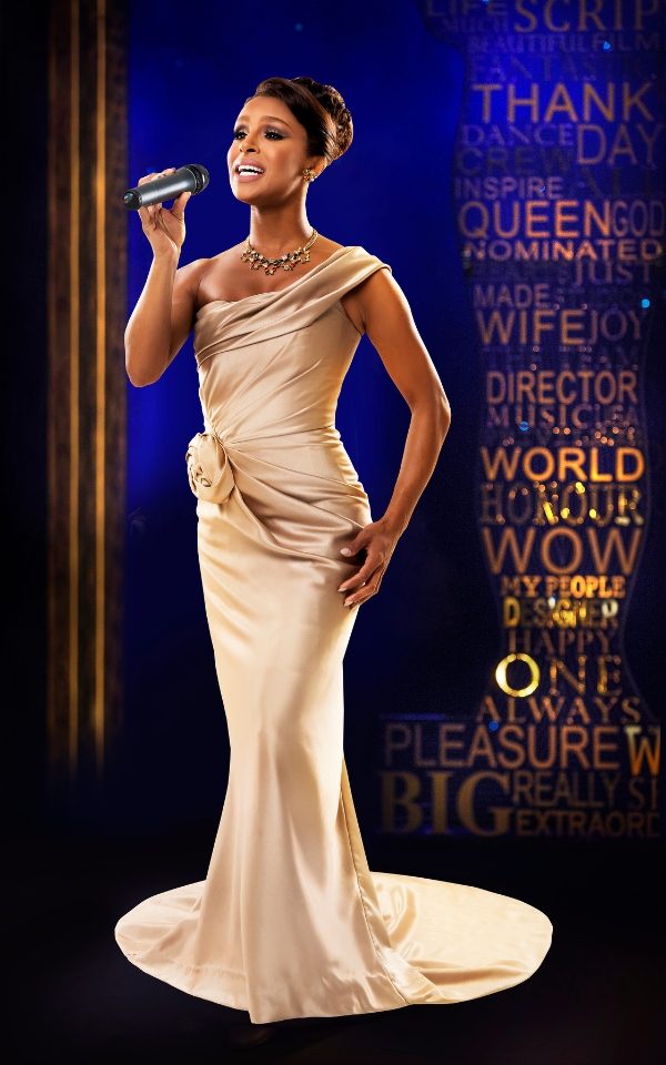 Melody Thornton as Rachel Marron in a light gold full-length dress singing into a microphone