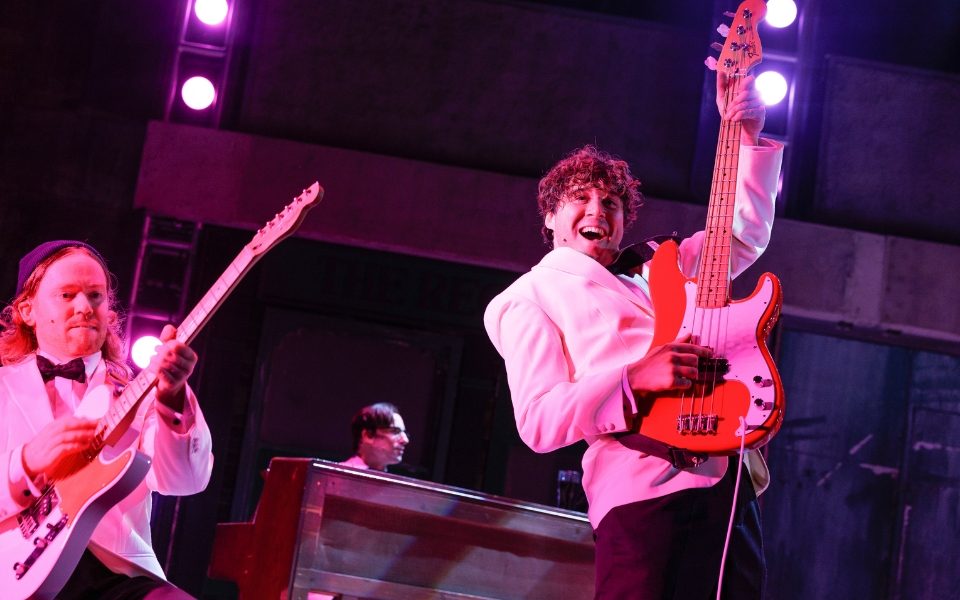 Two men in white suits playing electric guitars.