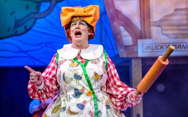 Simon Nock as the panto dame in an apron with chickens on holding up a rolling pin.