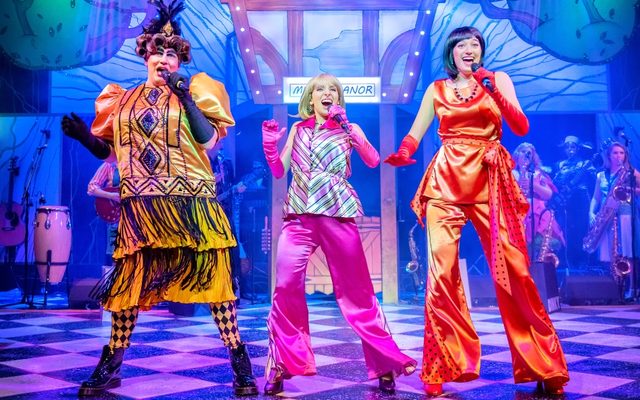 Three people singing in colourful panto costumes.