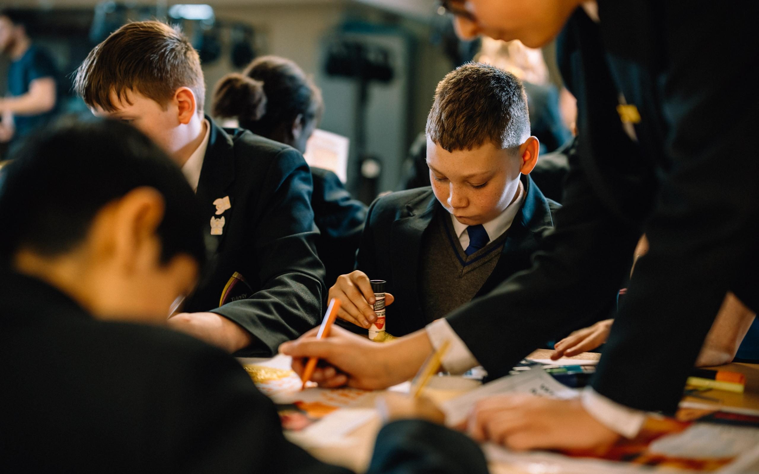 A group of secondary schoolchildren sit around a desk drawing, sticking and adding details to their mood board
