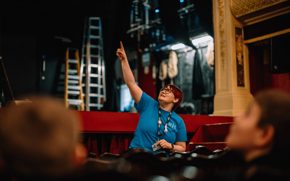 A member of the Learning & Engagement team points to the ceiling during a theatre tour of City Varieties Music Hall