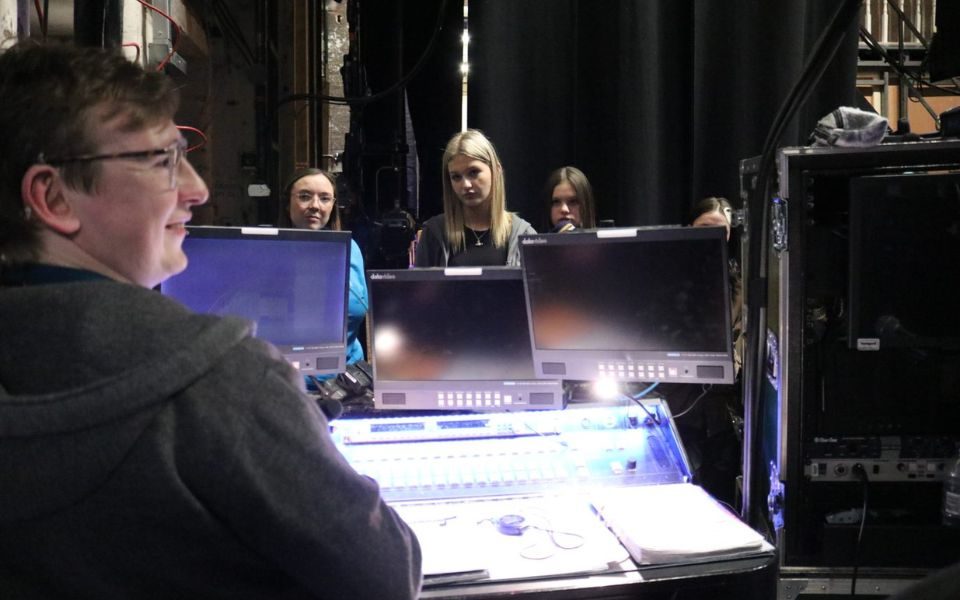 Backstage, students huddle around a tech desk as Sean delivers a tech talk.