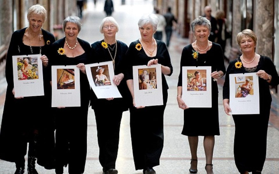 The Calendar Girls (LtoR) Tricia Stewart, Angela Baker, Beryl Bamforth, Lynda Logan, Chris Clancy and Ros Fawcett. They are all holding their calendar month. All the women also have sunflowers pinned on their black outfits.