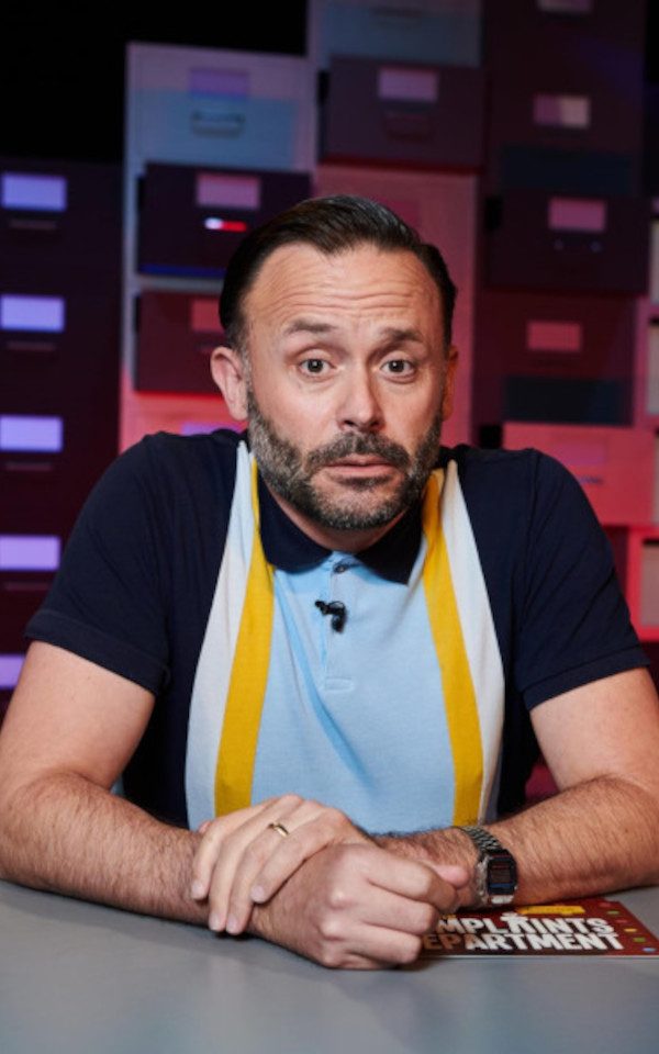 Geoff Norcott sits behind an office desk with a background of filing cabinets.