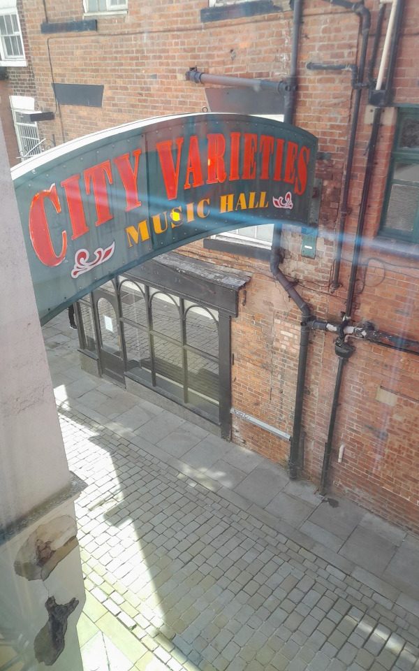 The City Varieties arch which sits across Swan Lane outside of the theatre. It is green metal with City Varieties Music Hall written in red and yellow.