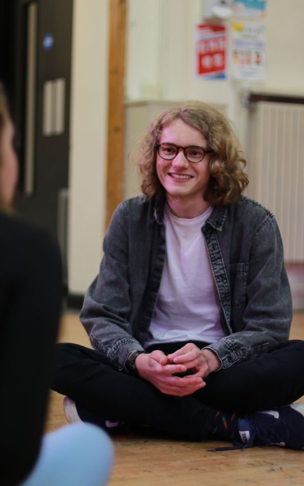 Gabe is sat cross-legged on the floor in rehearsals for LGYT. Credit: Kerry Maule